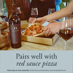 A bottle of Harvey & Harriet Wines and a slice of pepperoni pizza in a cardboard box on a dining table, with wine glasses and people reaching in. A text banner at the bottom reads 'Pairs well with red sauce pizza'.