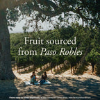 A scenic outdoor vineyard path with large trees casting dappled shadows, two people sitting on a blanket in the distance, and overlaid text reading 'Fruit sourced from Paso Robles' with a small footer note for Harvey and Harriet Wines.