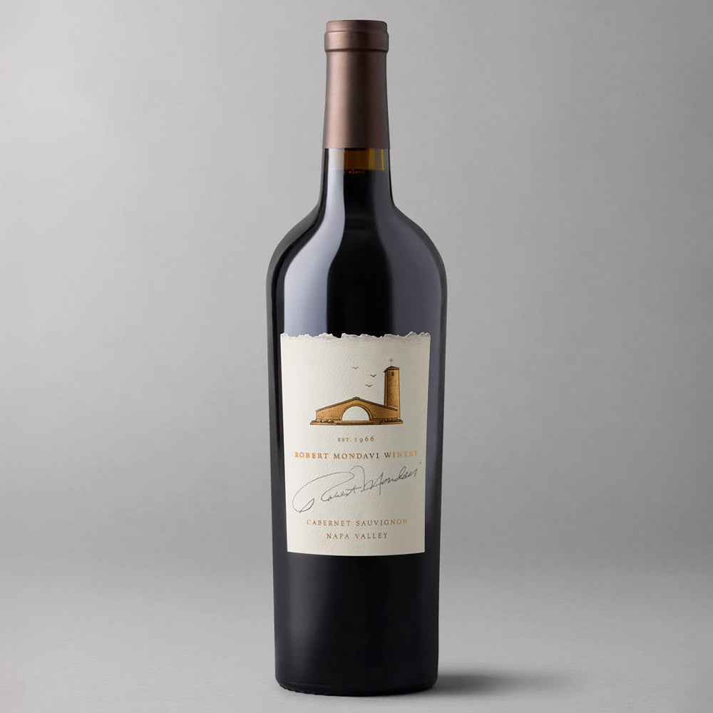 A single bottle of Robert Mondavi Winery Cabernet Sauvignon from Napa Valley, featuring a cream-colored label with a brown illustration of a vineyard and a dark glass bottle under a brown foil capsule, set against a neutral gray background.