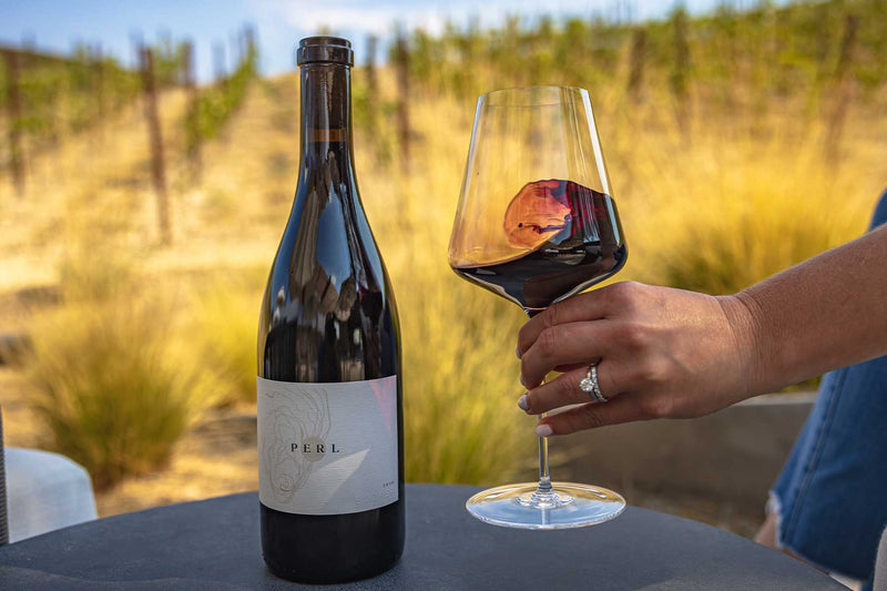 A bottle of Booker Perl next to a woman swirling wine in a glass.